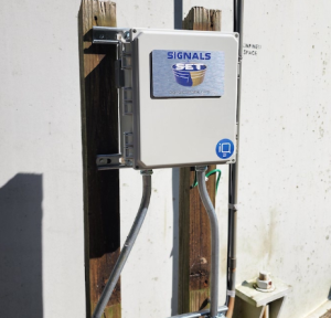 Signals-branded control enclosure mounted on wooden posts with conduit running to a concrete wall.