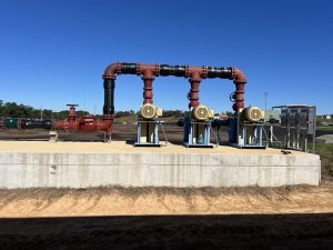 Three industrial pumps with large red-and-black pipe manifold.