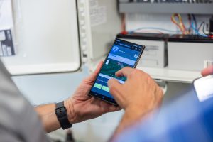 Two people interact with a smartphone displaying a map interface, possibly for navigation or monitoring.